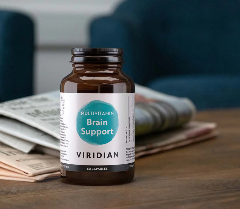 A bottle of viridian brain support multivitamin capsules on a side table with a folded newspaper
