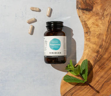 Viridian peppermint extract bottle with capsules and a mint leaf on a wooden surface.