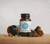 A bottle of viridian pine bark extract on a wooden surface with pine bark and capsules