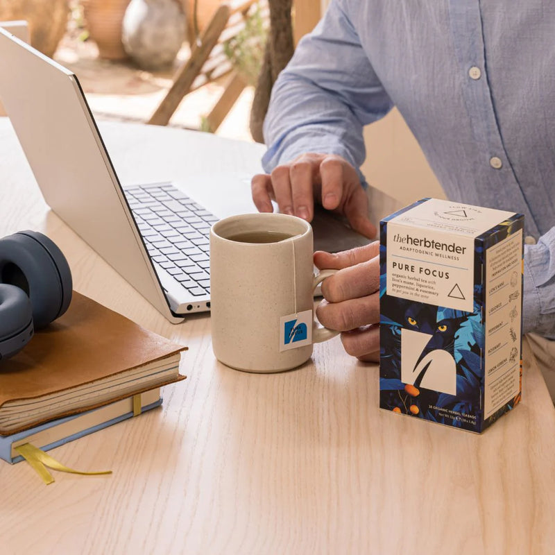 Person holding a mug with a laptop and notebook on a desk, next to a box of &