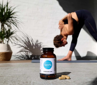 Bottle of Viridian Sports Formula supplement on a concrete surface with a person stretching in the background.