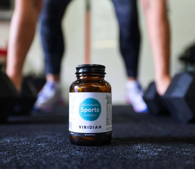 Bottle of Viridian Sports Formula on a gym floor with blurred gym-goers in the background