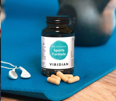 Multivitamin bottle labeled 'Sports Formula' by Viridian on a blue mat with scattered capsules.