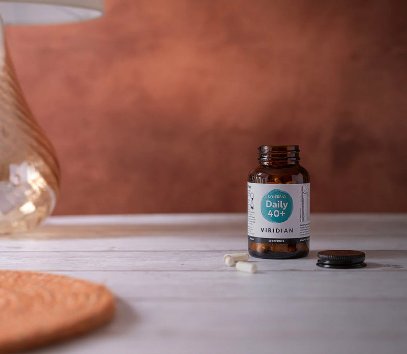 Bottle of Viridian Daily 40+ supplement on a wooden surface with a warm-toned background