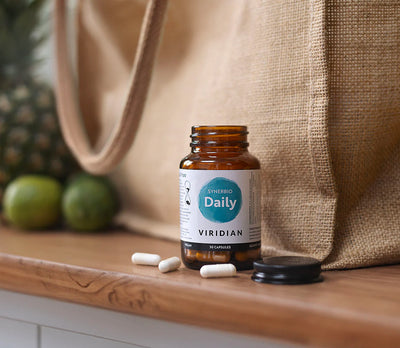 Viridian Daily supplement bottle on a wooden surface with a beige bag and green fruits in the background