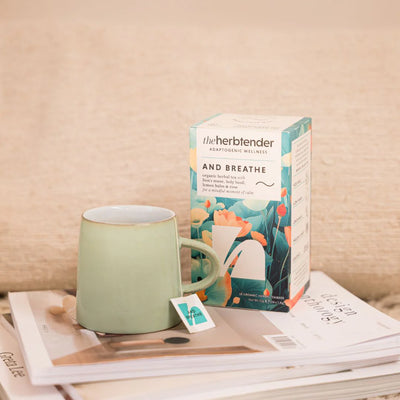 Tea mug and box of 'the herb tender' tea on a magazine with a beige background