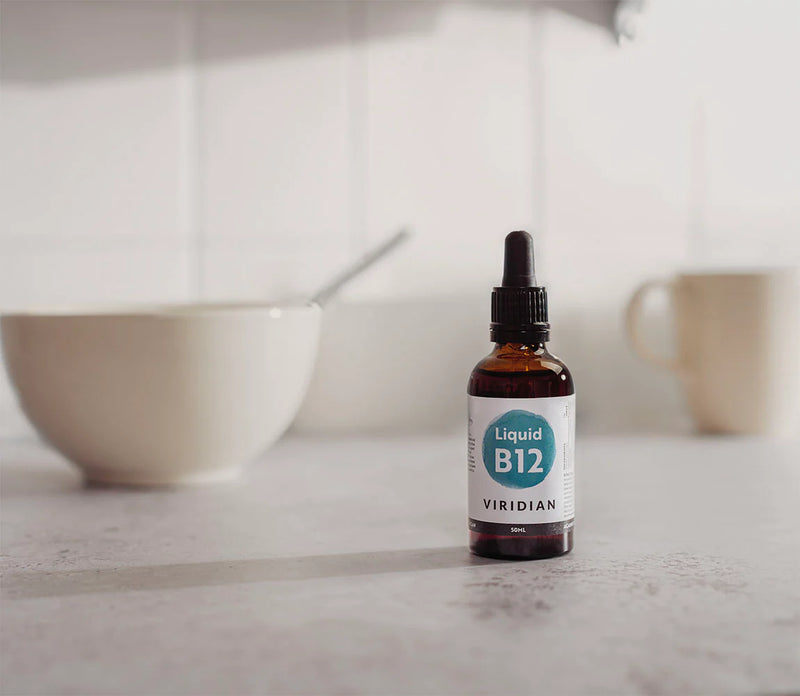 Bottle of Viridian Liquid B12 on a kitchen counter with a bowl and mug in the background.
