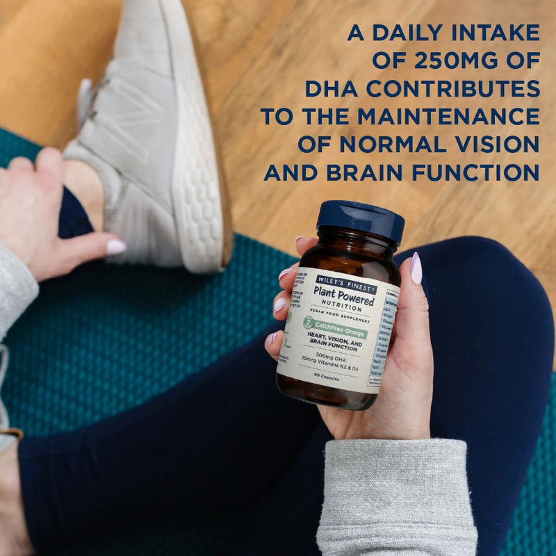 Person holding a bottle of supplements with text about DHA intake on a wooden floor.
