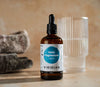 A bottle of Viridian Ionic Magnesium liquid supplement with a dropper, placed on a table with a glass and a scoop in the background.