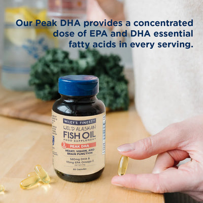 Fish oil supplement bottle with a hand holding a capsule on a wooden surface.