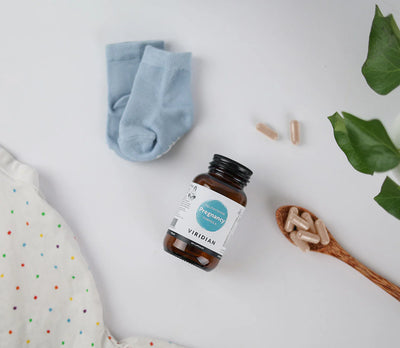 Supplement bottle with a label, blue socks, and a wooden spoon with capsules on a light background.