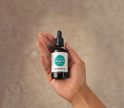 Hand holding a bottle of Viridian Organic Repair 5 with a blurred background