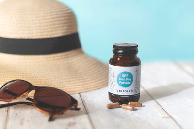 Bottle of Viridian supplements with sunglasses and a hat on a light surface with a blue background