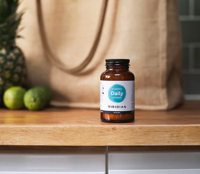Bottle of Viridian Daily Powder on a wooden surface with fruits in the background