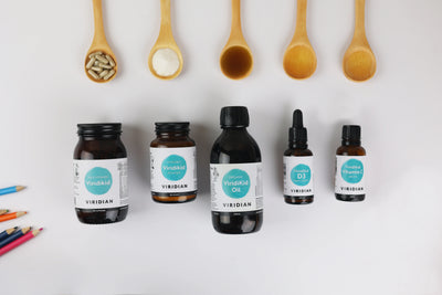 Collection of Viridian supplement bottles with wooden spoons and pencils on a white background