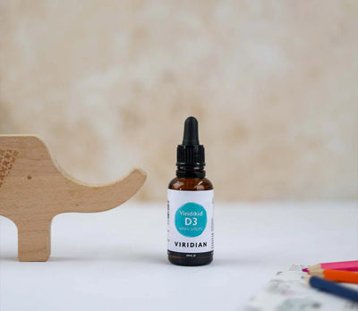 Bottle of Viridian D3 supplement on a white surface with a wooden toy and colorful pencils in the background.