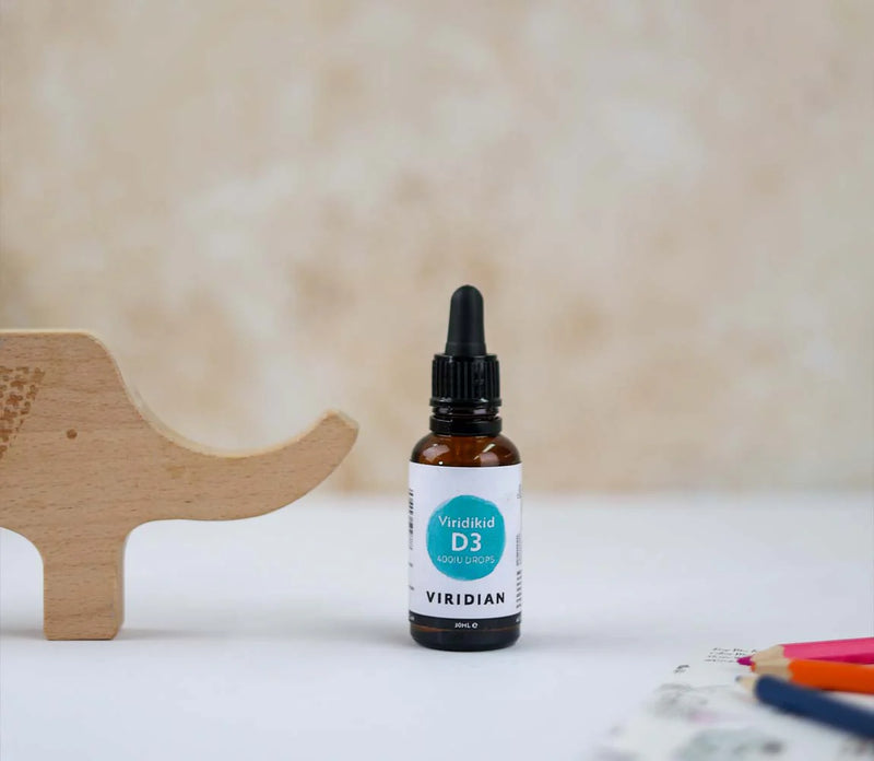 Bottle of Viridian D3 supplement on a white surface with a wooden toy and colorful pencils in the background.