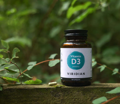 Viridian Vitamin D3 supplement bottle on a wooden surface with green foliage in the background