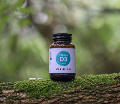 Viridian Vitamin D3 supplement bottle on a mossy log with a blurred natural background