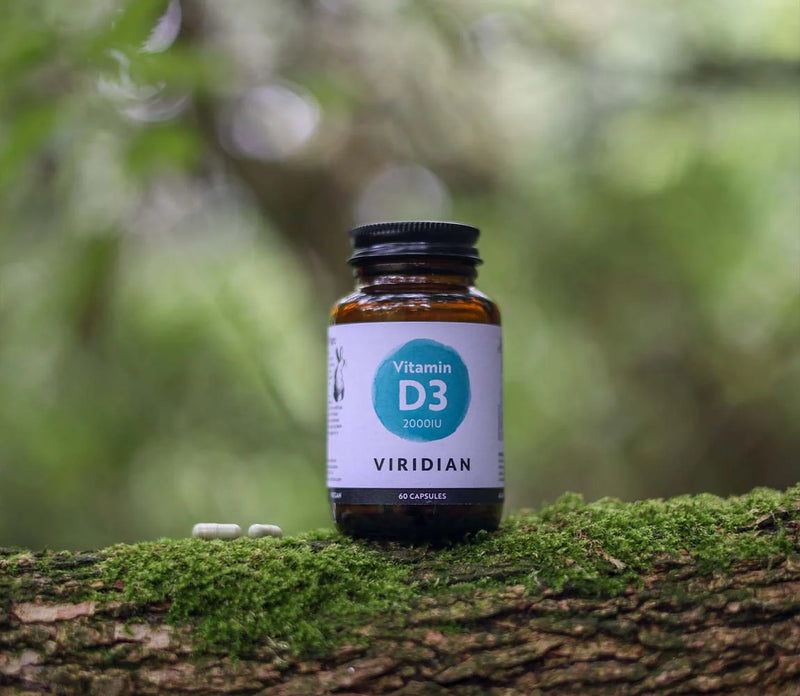 Viridian Vitamin D3 supplement bottle on a mossy log with a blurred natural background