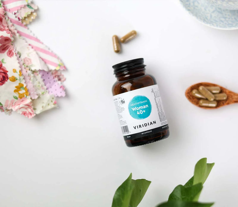 Bottle of Viridian supplements on a white surface with flowers and leaves.